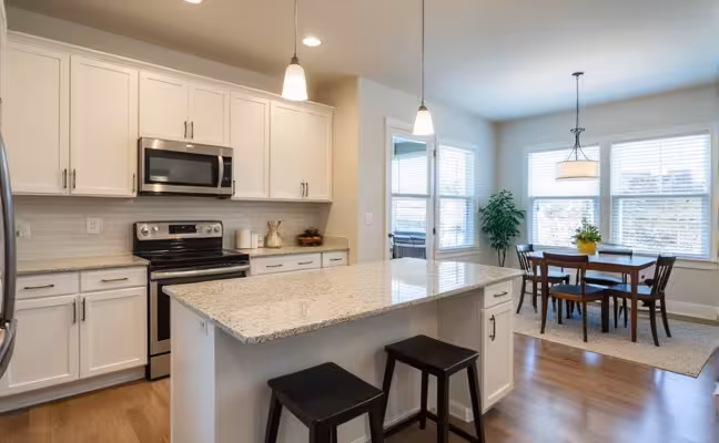 A bright, modern kitchen featuring stainless steel appliances, granite countertops, ample storage space, and an open layout that blends seamlessly with a dining area and living room showcasing a neutral color scheme