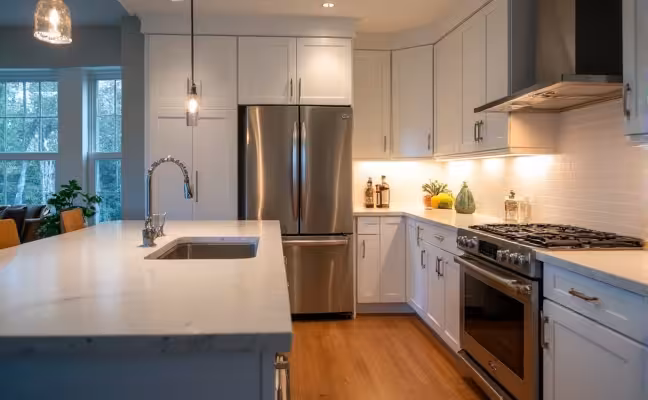A close-up of the work triangle in a modern kitchen, showing the sink, refrigerator, and stove in close proximity to each other, with quartz countertops and hardwood flooring, illuminated by a combination of task and ambient lighting